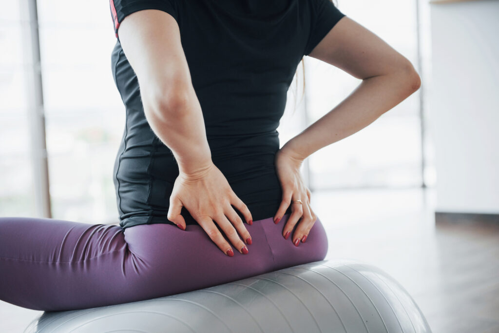 Pregnant woman sitting on an exercise ball holding her lower back, back pain Mast Health helps Tampa moms manage safely