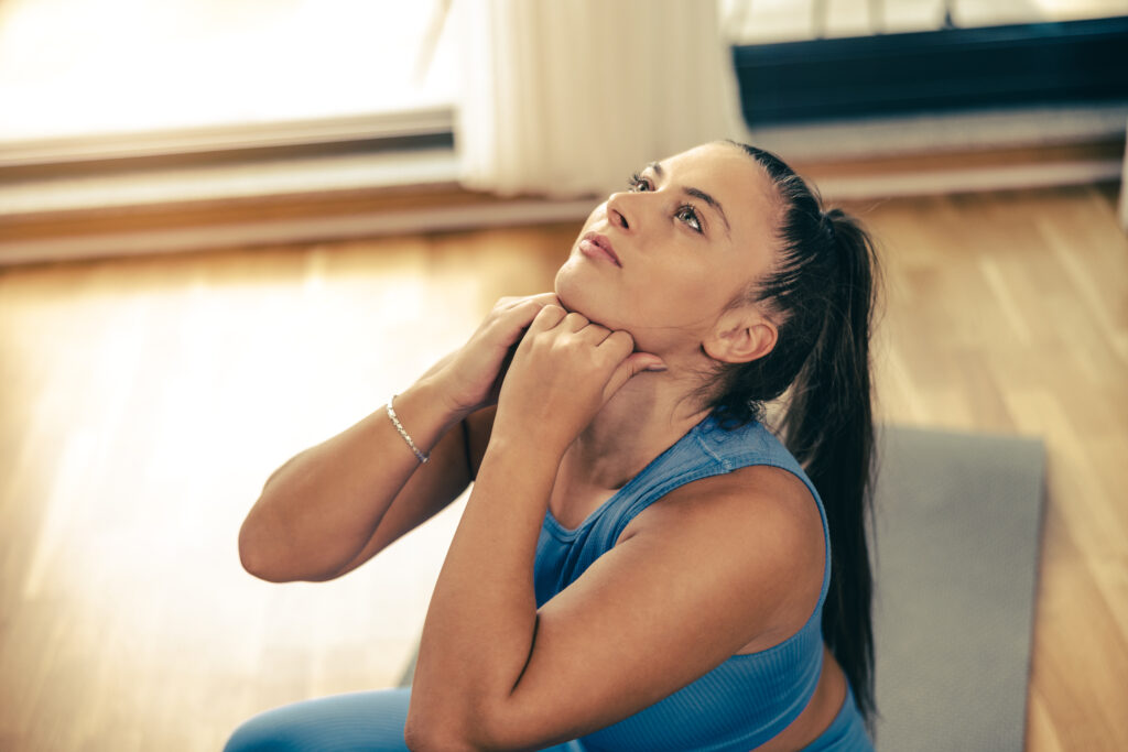 Young woman stretching her neck during a morning exercise routine at home to relieve neck pain, a technique recommended at Mast Health in Tampa, FL